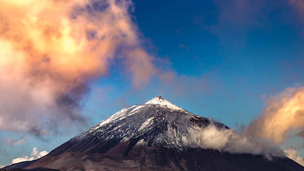 A breathtaking view of Mount Teide's snow-capped peak surrounded by vibrant sunset clouds.