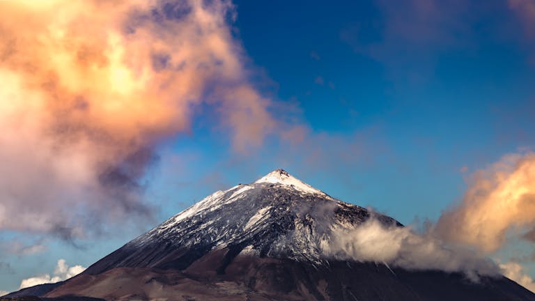 A breathtaking view of Mount Teide's snow-capped peak surrounded by vibrant sunset clouds.